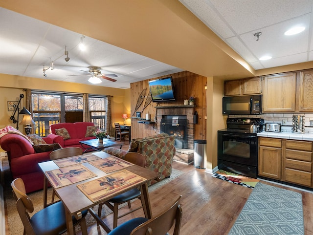 dining room with a fireplace, ceiling fan, wood walls, and light hardwood / wood-style flooring