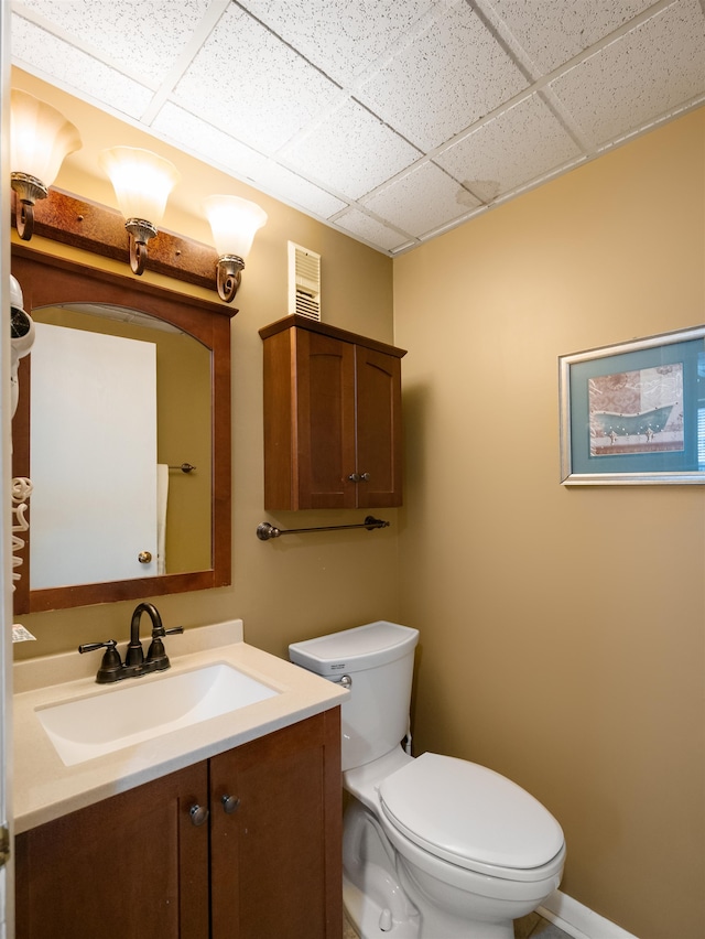 bathroom featuring toilet, vanity, and a drop ceiling