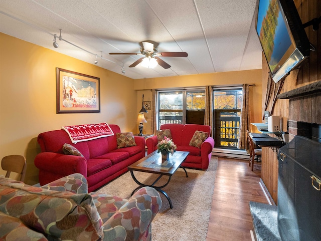 living room with a textured ceiling, hardwood / wood-style flooring, ceiling fan, and a baseboard heating unit