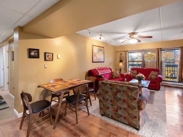 living room featuring wood-type flooring, ceiling fan, and a baseboard heating unit