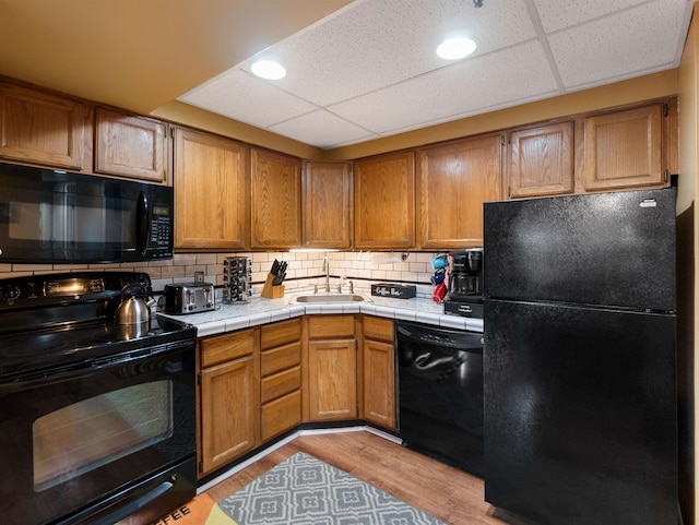 kitchen featuring sink, black appliances, tasteful backsplash, tile counters, and light wood-type flooring