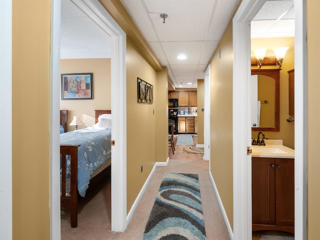 hall with light colored carpet, sink, and a drop ceiling