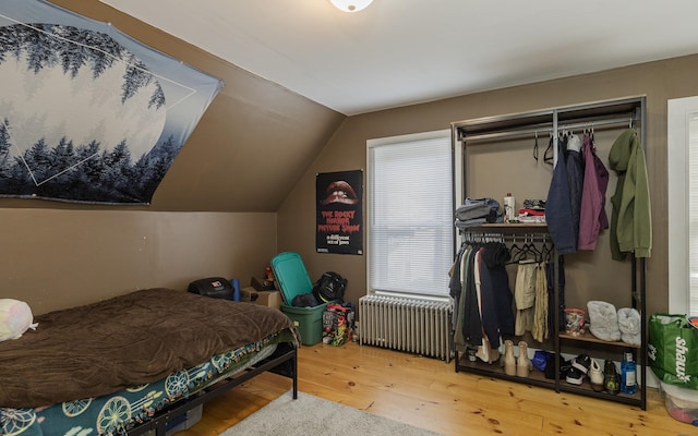 bedroom featuring radiator heating unit, hardwood / wood-style flooring, vaulted ceiling, and a closet