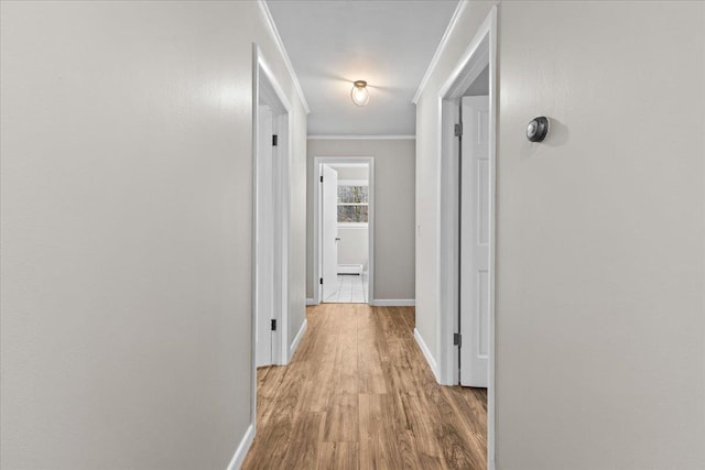 corridor with a baseboard heating unit, light hardwood / wood-style floors, and ornamental molding