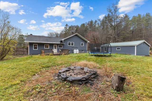 rear view of property with a lawn, a trampoline, a deck, and an outdoor fire pit