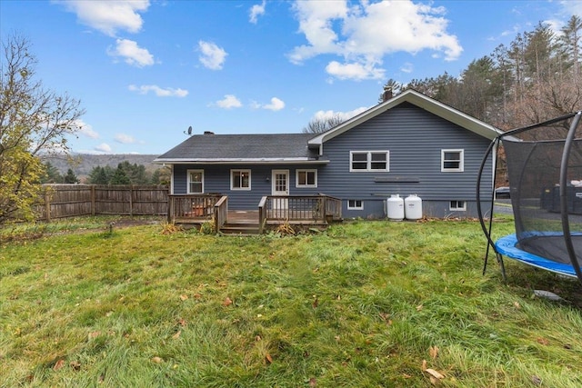 back of house with a trampoline, a lawn, and a wooden deck