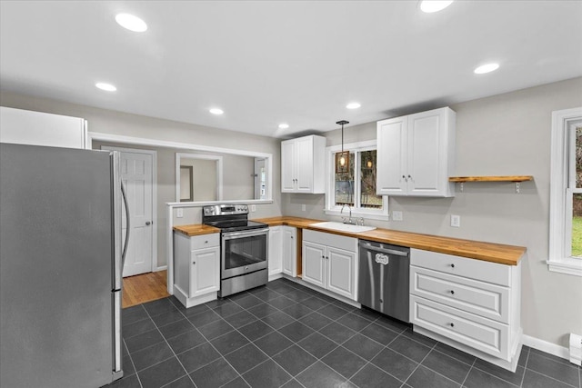 kitchen with stainless steel appliances, sink, white cabinets, butcher block countertops, and hanging light fixtures