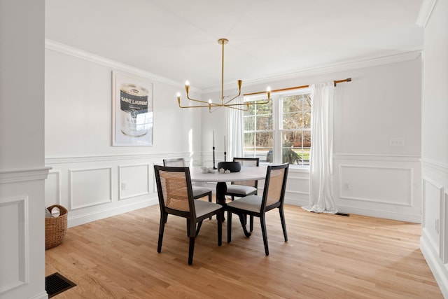 dining area with light hardwood / wood-style floors, an inviting chandelier, decorative columns, and ornamental molding