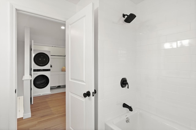 bathroom with tiled shower / bath, wood-type flooring, and stacked washer / dryer