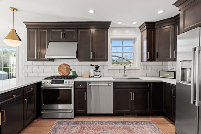 kitchen with sink, appliances with stainless steel finishes, extractor fan, decorative light fixtures, and wood-type flooring