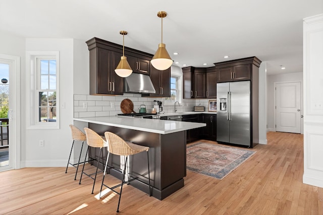 kitchen with a kitchen breakfast bar, light hardwood / wood-style flooring, kitchen peninsula, exhaust hood, and appliances with stainless steel finishes