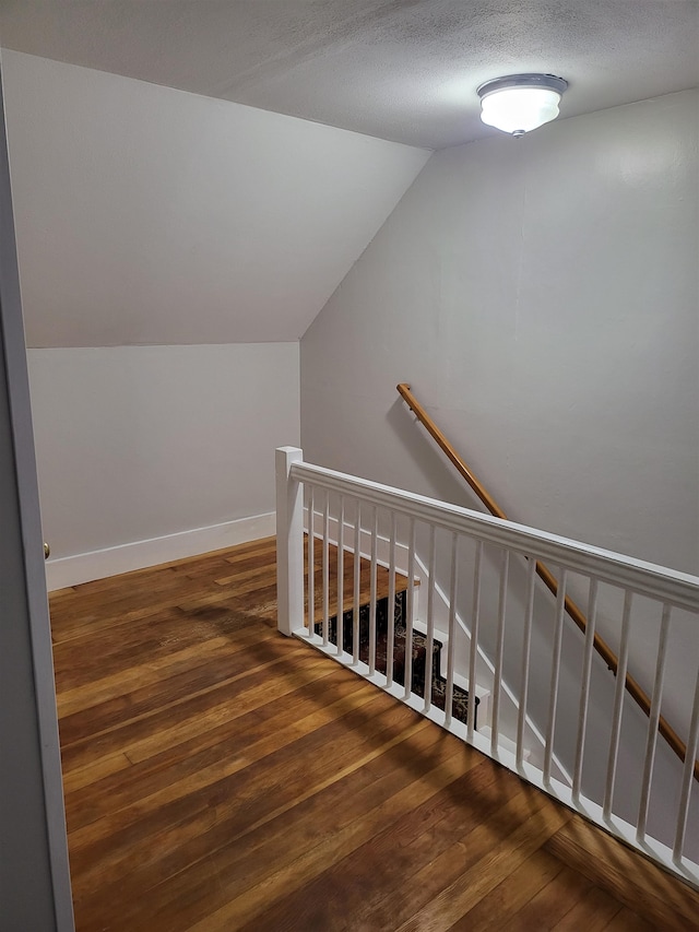 staircase with hardwood / wood-style floors, lofted ceiling, and a textured ceiling