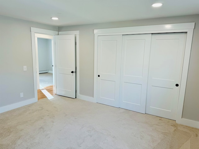 unfurnished bedroom featuring light colored carpet, a closet, and a baseboard heating unit