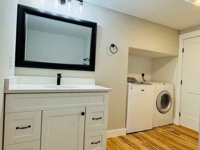 clothes washing area featuring sink, light hardwood / wood-style floors, and independent washer and dryer