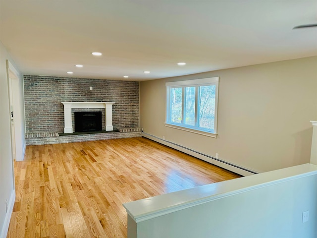 unfurnished living room featuring a fireplace, brick wall, a baseboard heating unit, and hardwood / wood-style flooring