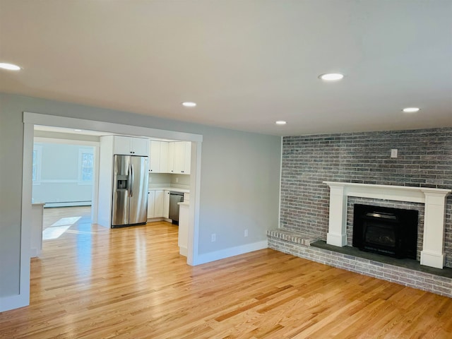 unfurnished living room with light wood-type flooring, a fireplace, and a baseboard radiator