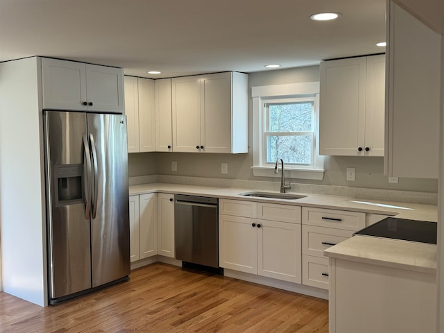 kitchen with white cabinets, appliances with stainless steel finishes, light hardwood / wood-style flooring, and sink