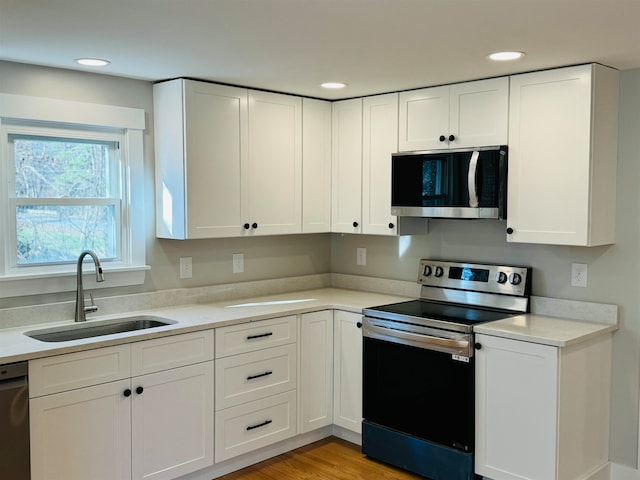 kitchen with sink, white cabinetry, stainless steel appliances, and light hardwood / wood-style flooring