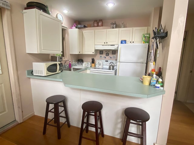 kitchen featuring a kitchen breakfast bar, white appliances, and white cabinetry