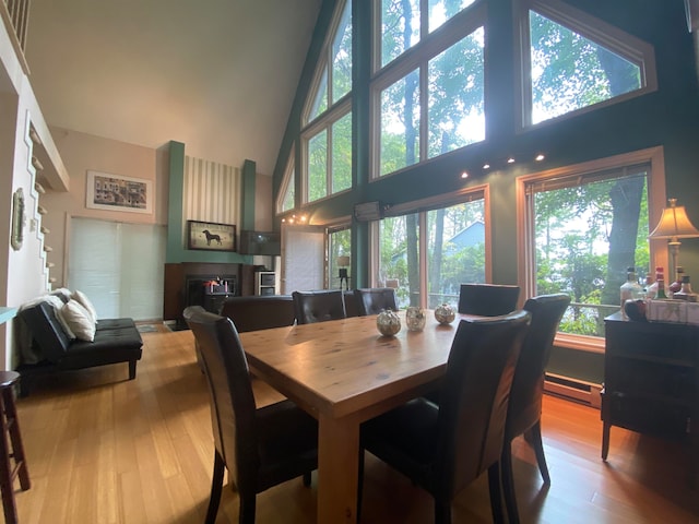 dining space with light hardwood / wood-style flooring, high vaulted ceiling, and a baseboard heating unit