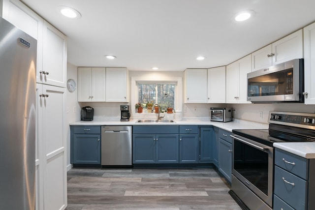 kitchen with blue cabinets, sink, stainless steel appliances, and white cabinetry