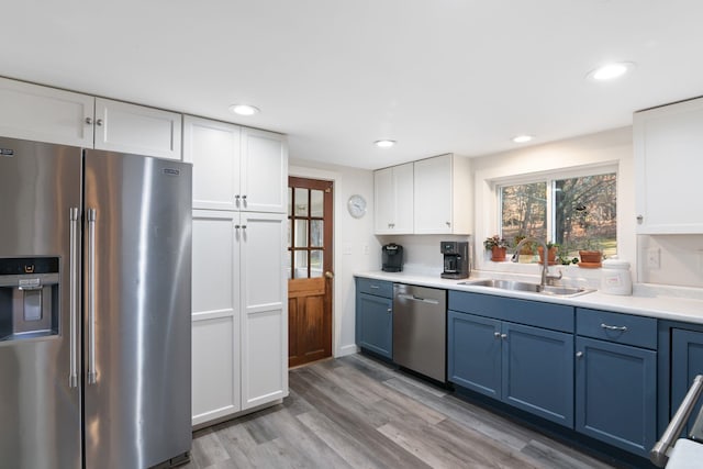 kitchen with white cabinets, appliances with stainless steel finishes, sink, light wood-type flooring, and blue cabinets