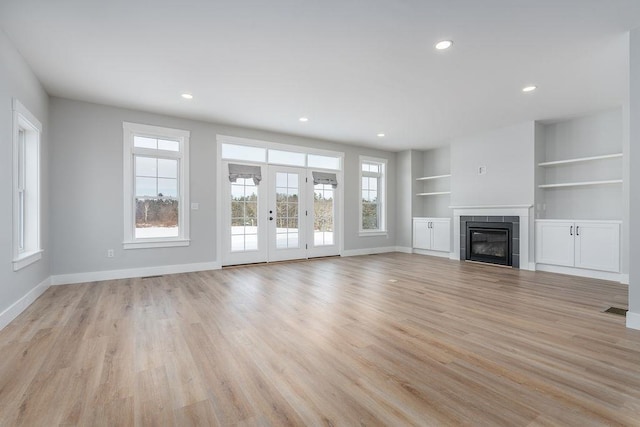 unfurnished living room featuring a tile fireplace, a wealth of natural light, built in features, and light wood-type flooring