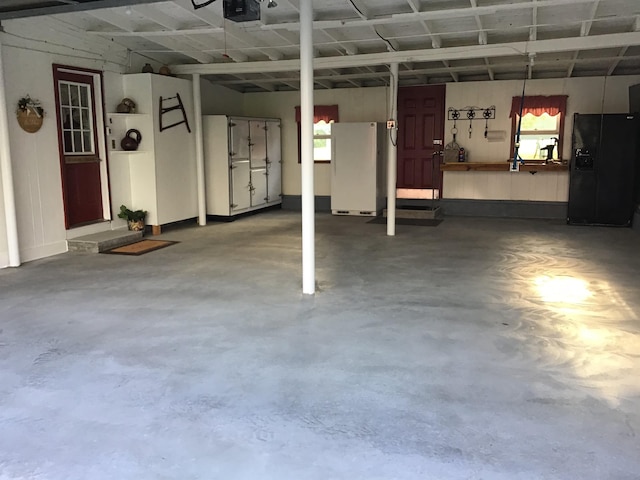 garage with black refrigerator with ice dispenser, white fridge, and a garage door opener