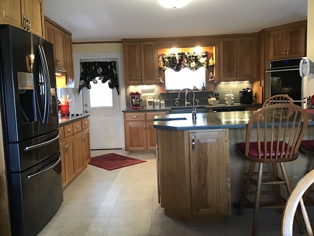 kitchen featuring sink, a breakfast bar, light tile patterned floors, black appliances, and a center island with sink