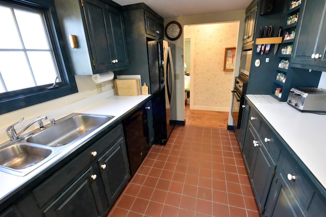 kitchen with black oven, stainless steel fridge, sink, and tile patterned flooring