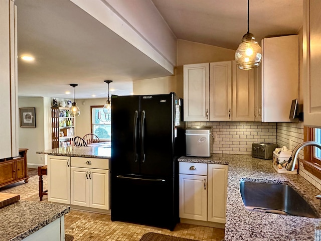 kitchen featuring black refrigerator, decorative light fixtures, white cabinets, and sink