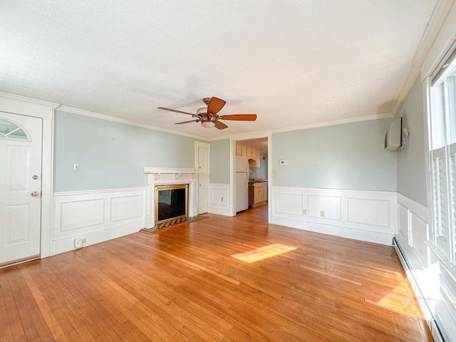 unfurnished living room featuring ceiling fan, a baseboard radiator, light hardwood / wood-style flooring, a fireplace, and ornamental molding