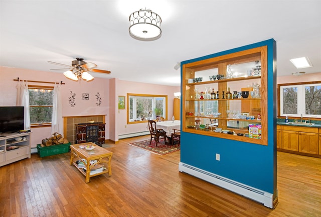 living room with a wealth of natural light, light hardwood / wood-style flooring, ceiling fan, and a baseboard heating unit