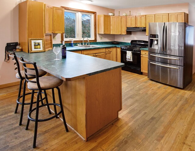 kitchen with kitchen peninsula, stainless steel refrigerator with ice dispenser, light wood-type flooring, sink, and black gas range