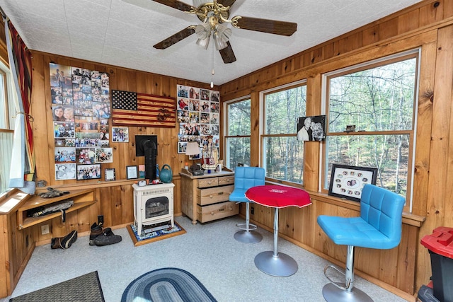 interior space featuring a wood stove, wood walls, and ceiling fan