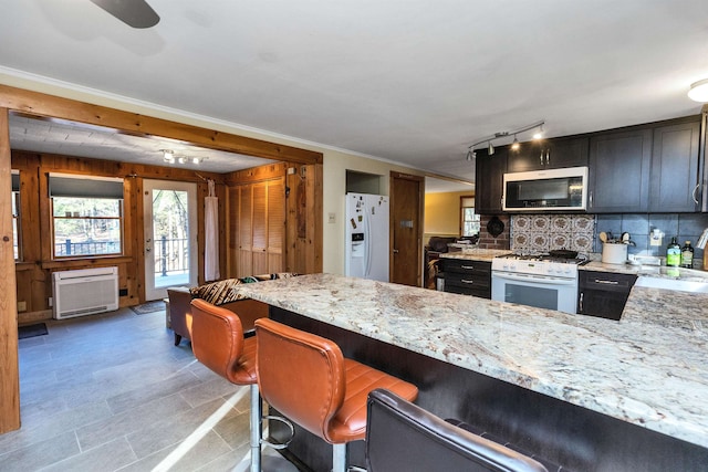 kitchen featuring white appliances, crown molding, decorative backsplash, light stone countertops, and a breakfast bar area