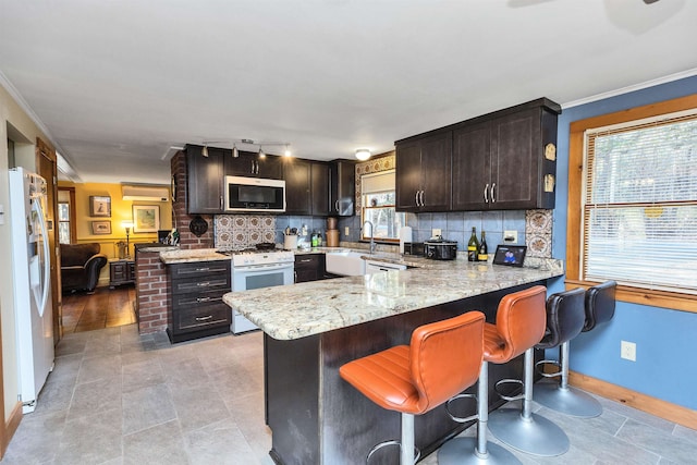 kitchen with dark brown cabinetry, white appliances, kitchen peninsula, and tasteful backsplash