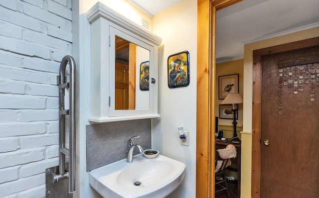 bathroom with decorative backsplash, crown molding, sink, and brick wall