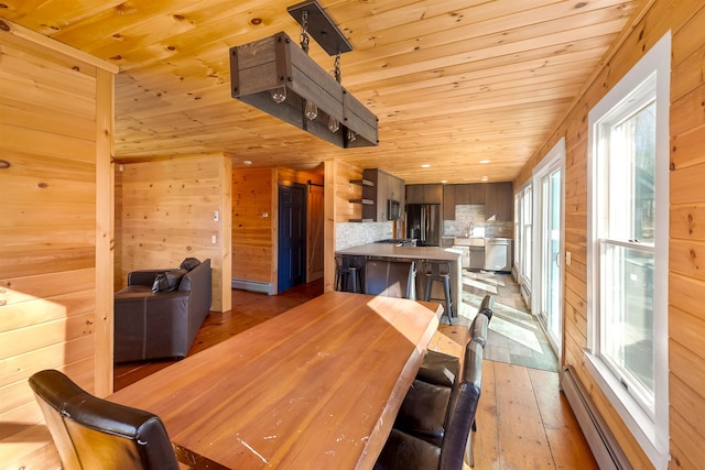 dining area with wood walls, wood ceiling, a baseboard heating unit, and light wood-type flooring