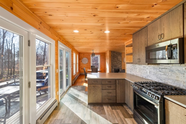 kitchen featuring a baseboard heating unit, kitchen peninsula, light hardwood / wood-style floors, decorative backsplash, and appliances with stainless steel finishes