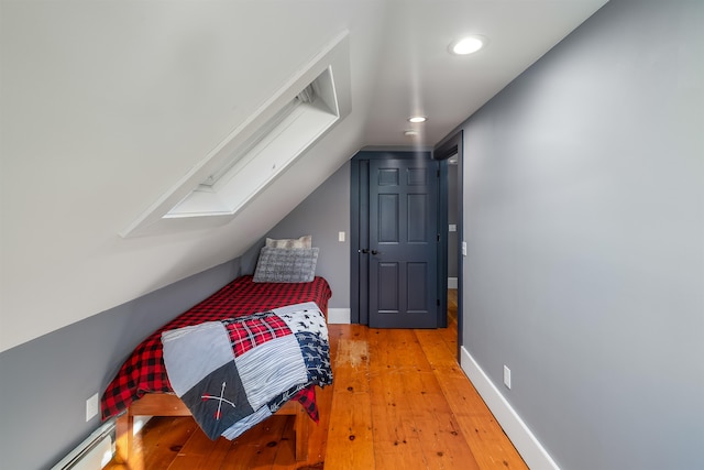 bedroom with baseboard heating, lofted ceiling with skylight, and hardwood / wood-style floors