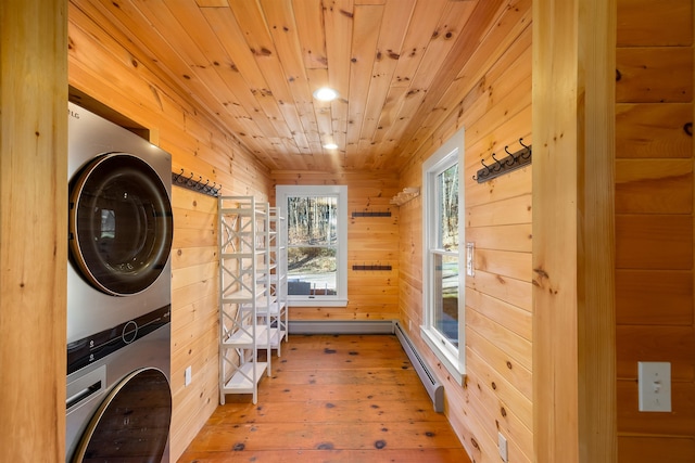 washroom with wooden walls, light wood-type flooring, a baseboard radiator, stacked washer / drying machine, and wood ceiling