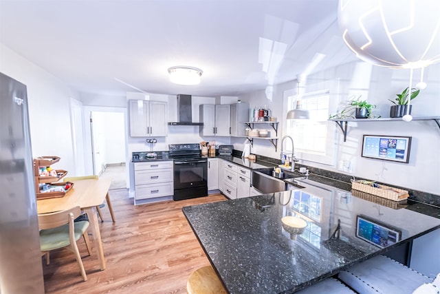 kitchen with stainless steel fridge, sink, wall chimney range hood, light hardwood / wood-style floors, and black range with electric stovetop