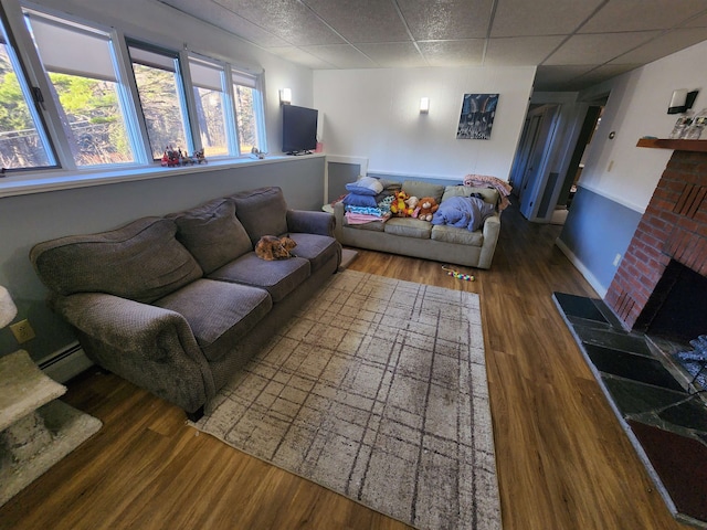 living room featuring a drop ceiling, a brick fireplace, dark wood-type flooring, and baseboard heating