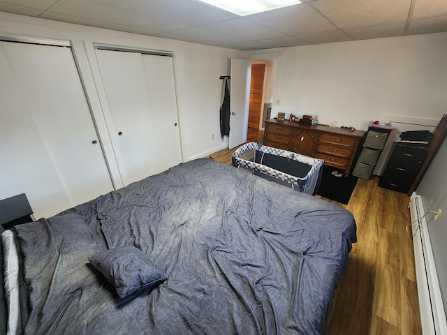 bedroom featuring multiple closets, a paneled ceiling, dark hardwood / wood-style floors, and a baseboard radiator