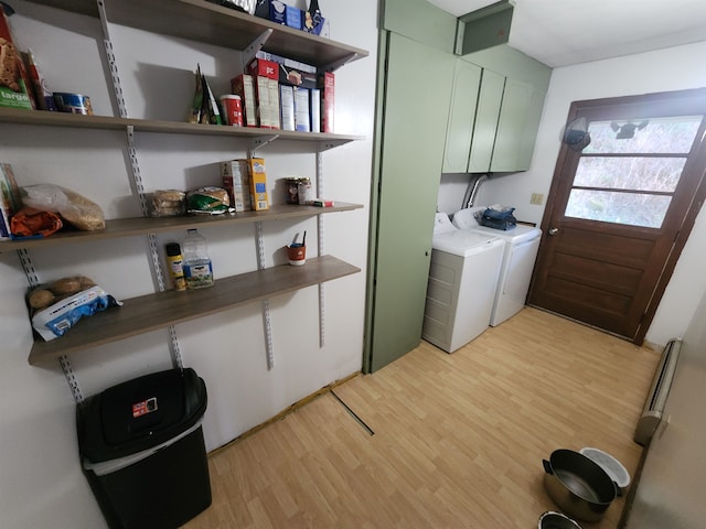 laundry room featuring cabinets, washing machine and dryer, a baseboard heating unit, and light hardwood / wood-style flooring