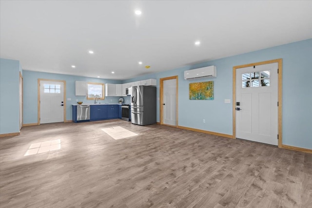 unfurnished living room featuring a wall mounted AC, sink, and light hardwood / wood-style floors