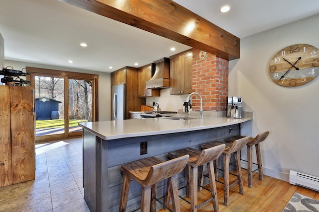 kitchen with kitchen peninsula, custom exhaust hood, a baseboard radiator, light hardwood / wood-style floors, and stainless steel refrigerator