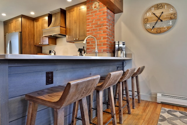 kitchen with a kitchen breakfast bar, light hardwood / wood-style flooring, baseboard heating, custom range hood, and stainless steel refrigerator