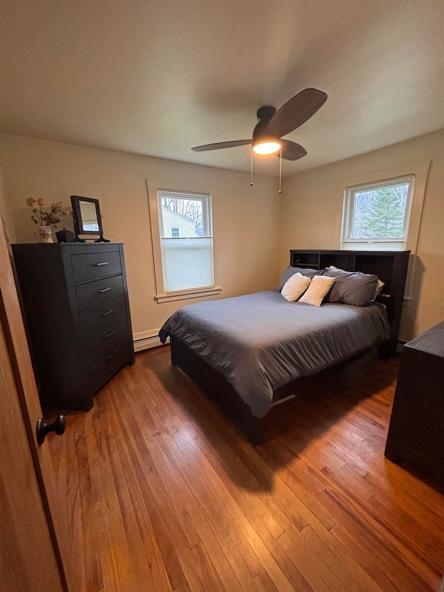 bedroom with baseboard heating, ceiling fan, and dark hardwood / wood-style floors